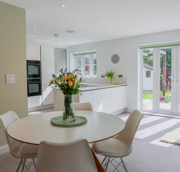 White handleless open-plan kitchen with dining area, garden doors and light neutral finishes